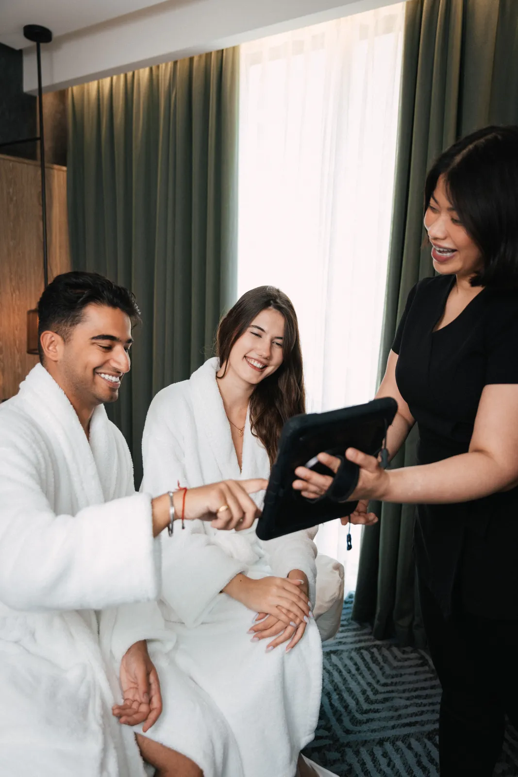 Two guests in robes choosing a treatment on a tablet with a therapist