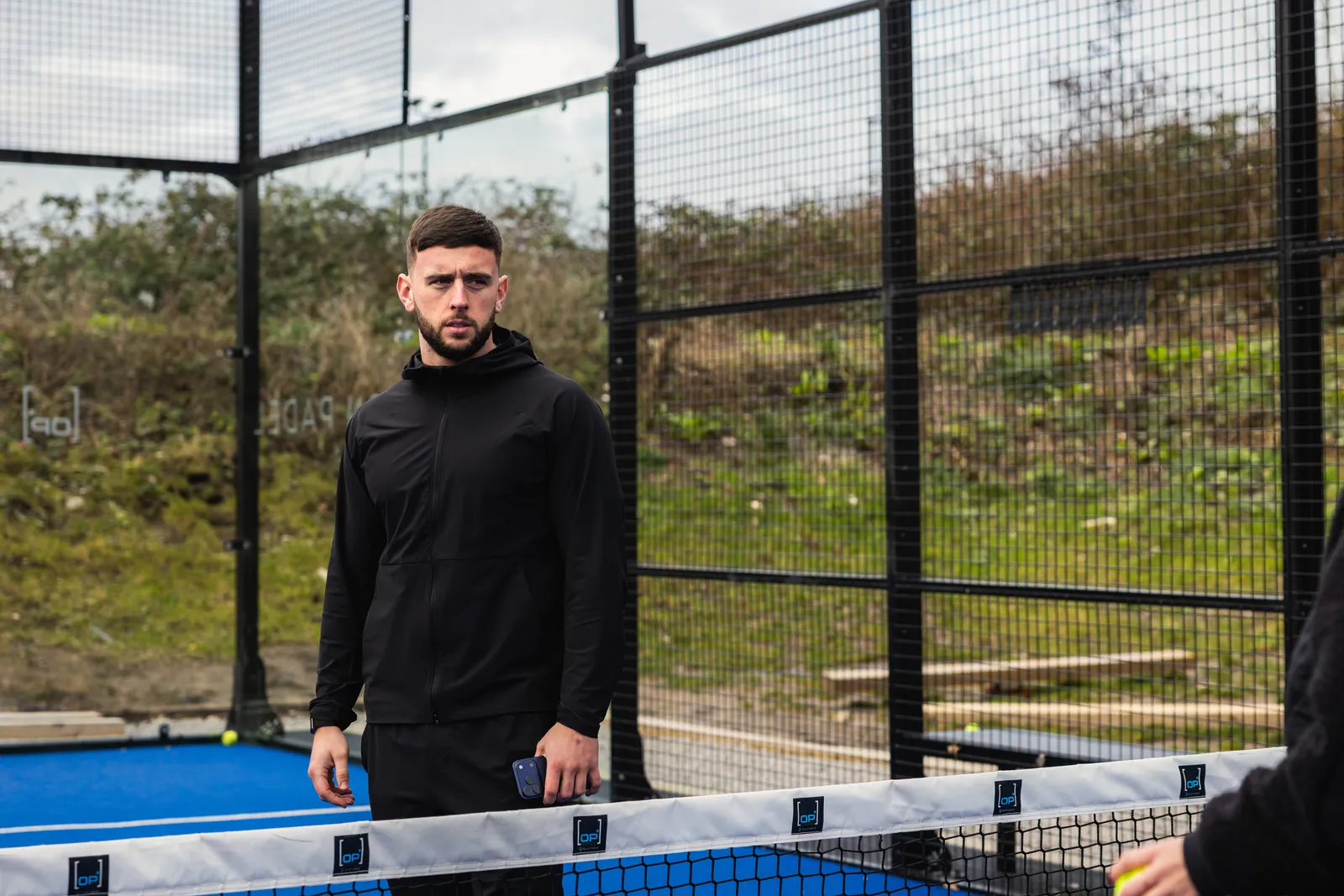 A coach standing at the net on an outdoor padel court