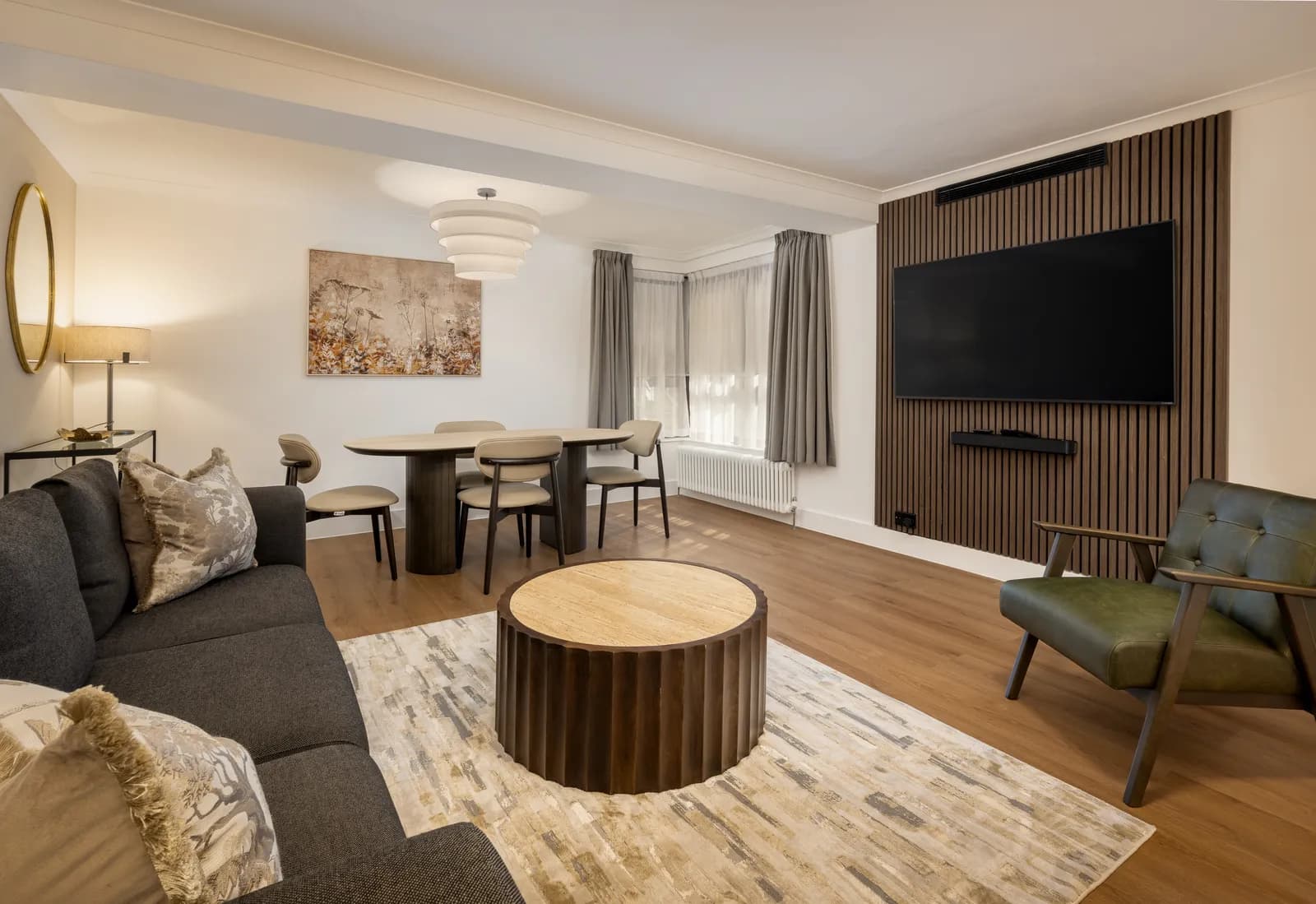 A serviced apartment lounge with a dining table and a wood-panelled TV wall